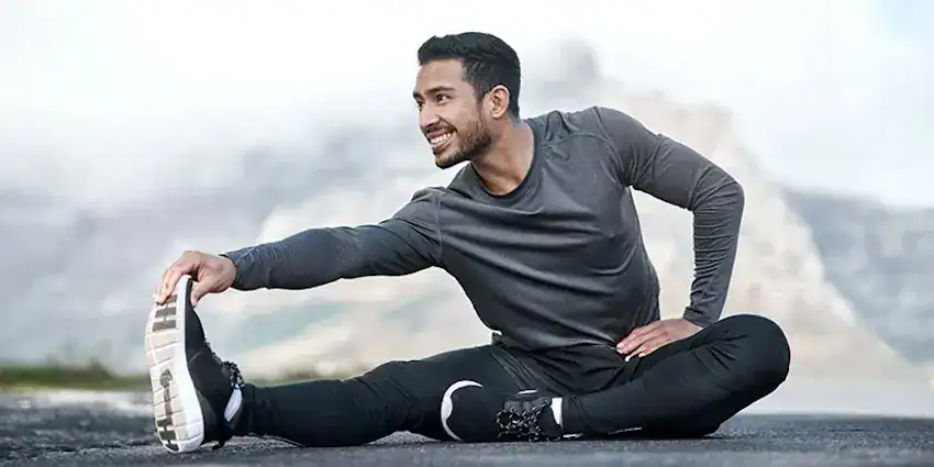 A man performing a seated hamstring stretch outdoors on a paved surface.