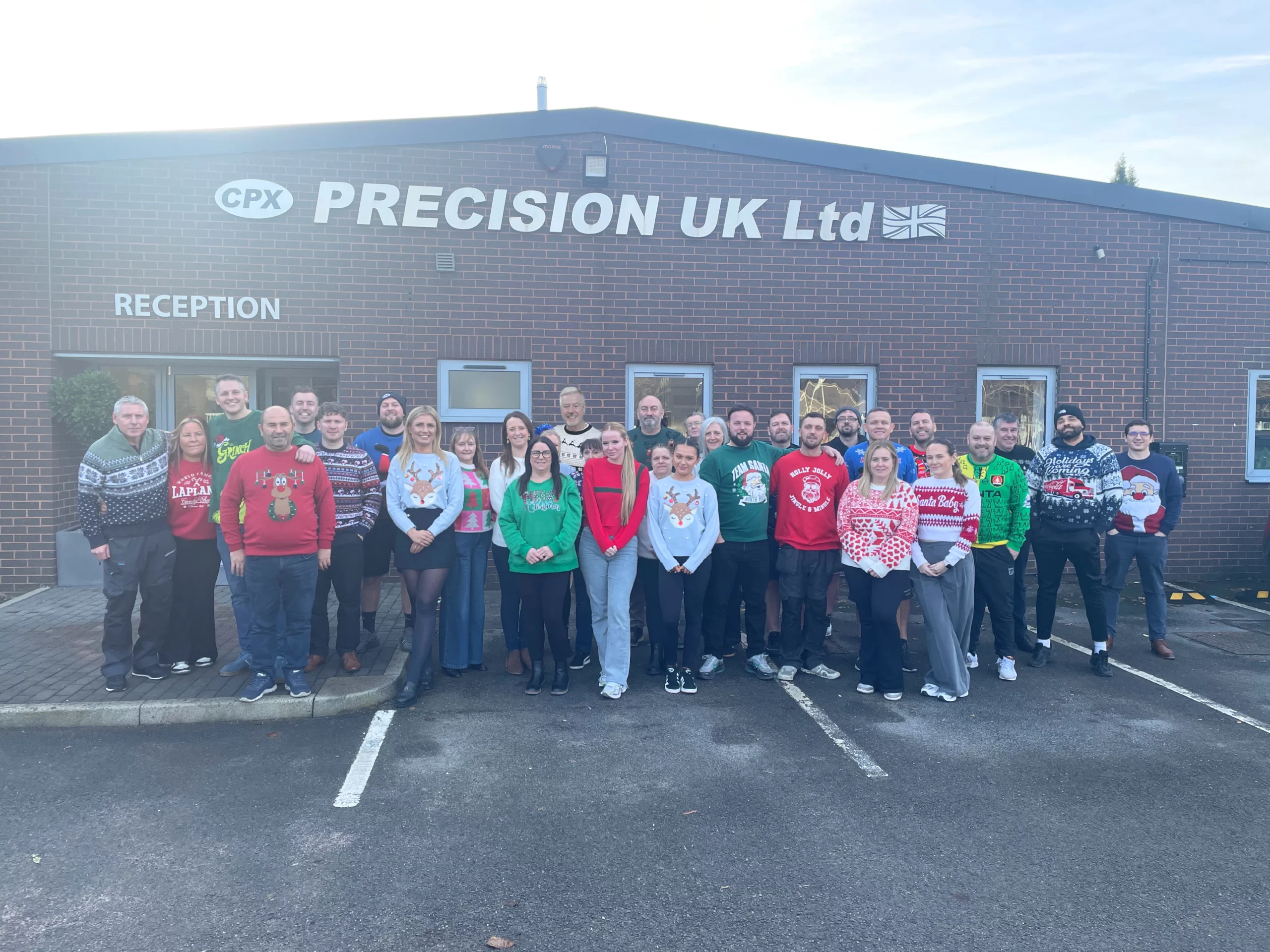 CPX Team wearing Christmas Jumpers standing outside of our Headquarters, below the logo "CPX Precision UK"