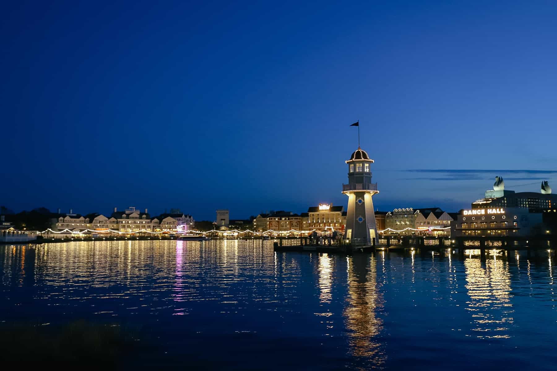 the Epcot Resorts area at night with the lighthouse sitting at the dock on the lake