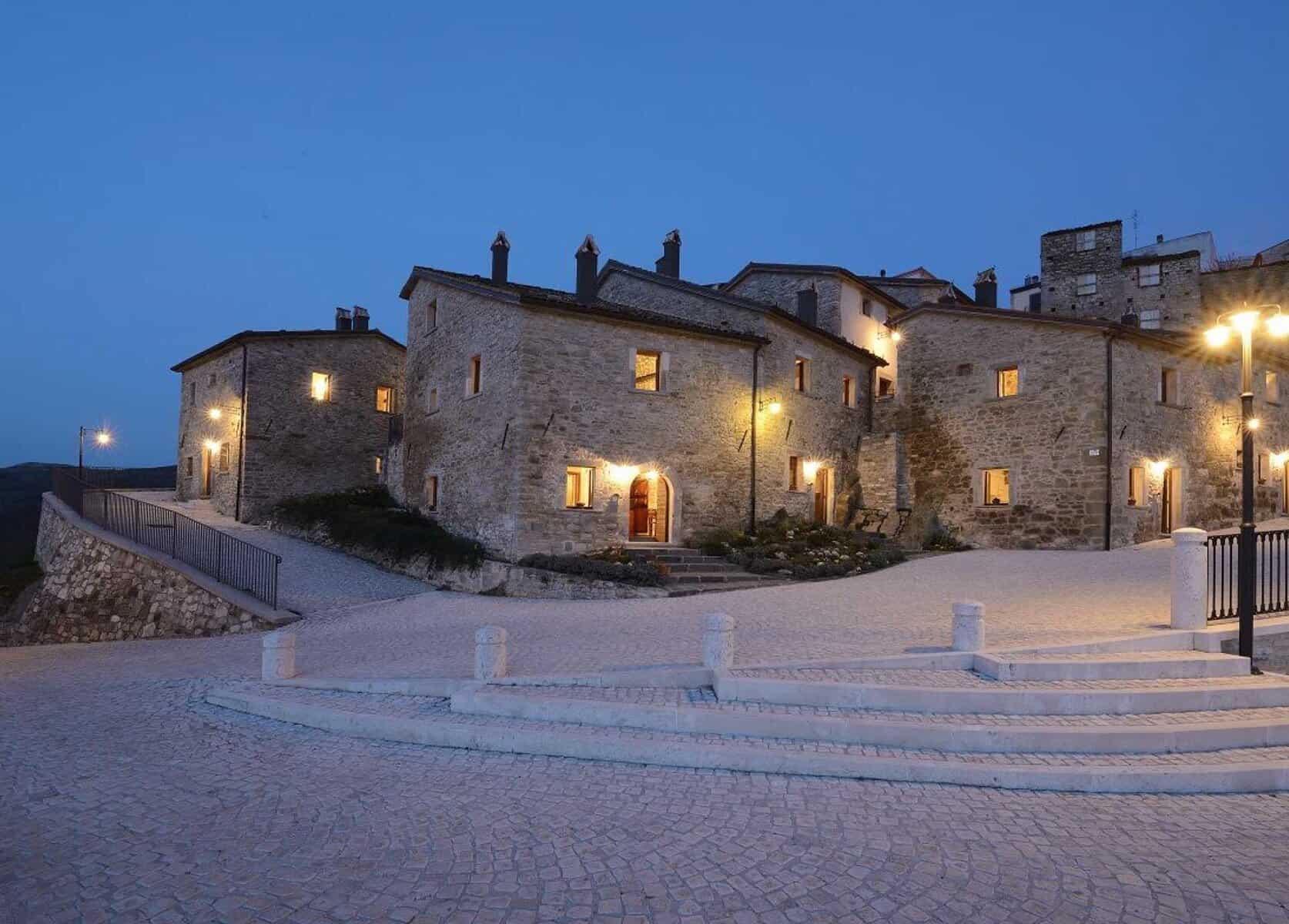 Vecchio borgo in pietra di notte con illuminazione calda, strada pavimentata e scale. Atmosfera suggestiva, perfetta per soggiorni romantici e vacanze in Toscana, Italia. Design e charme autentico.