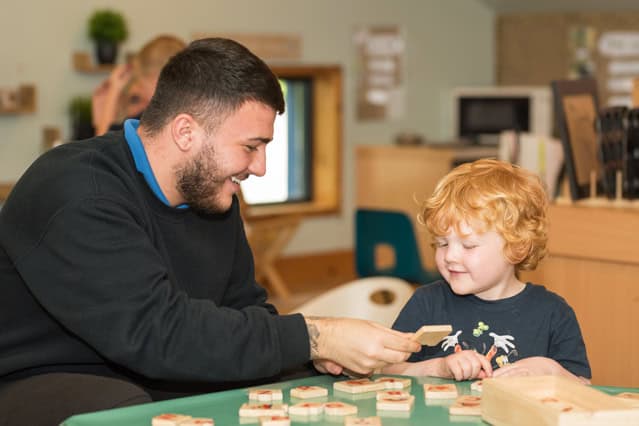 A young man engaging with a curly-haired child in a colourful childcare setting, promoting early childhood education and play-based learning at Thrive Childcare.