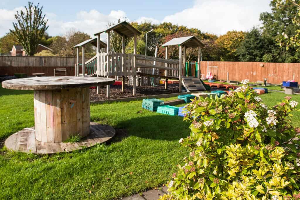 Colourful outdoor nursery play area at Thrive Childcare with wooden play structures, balanced rocks, and vibrant garden scenery, offering a safe and engaging environment for children’s outdoor activities.