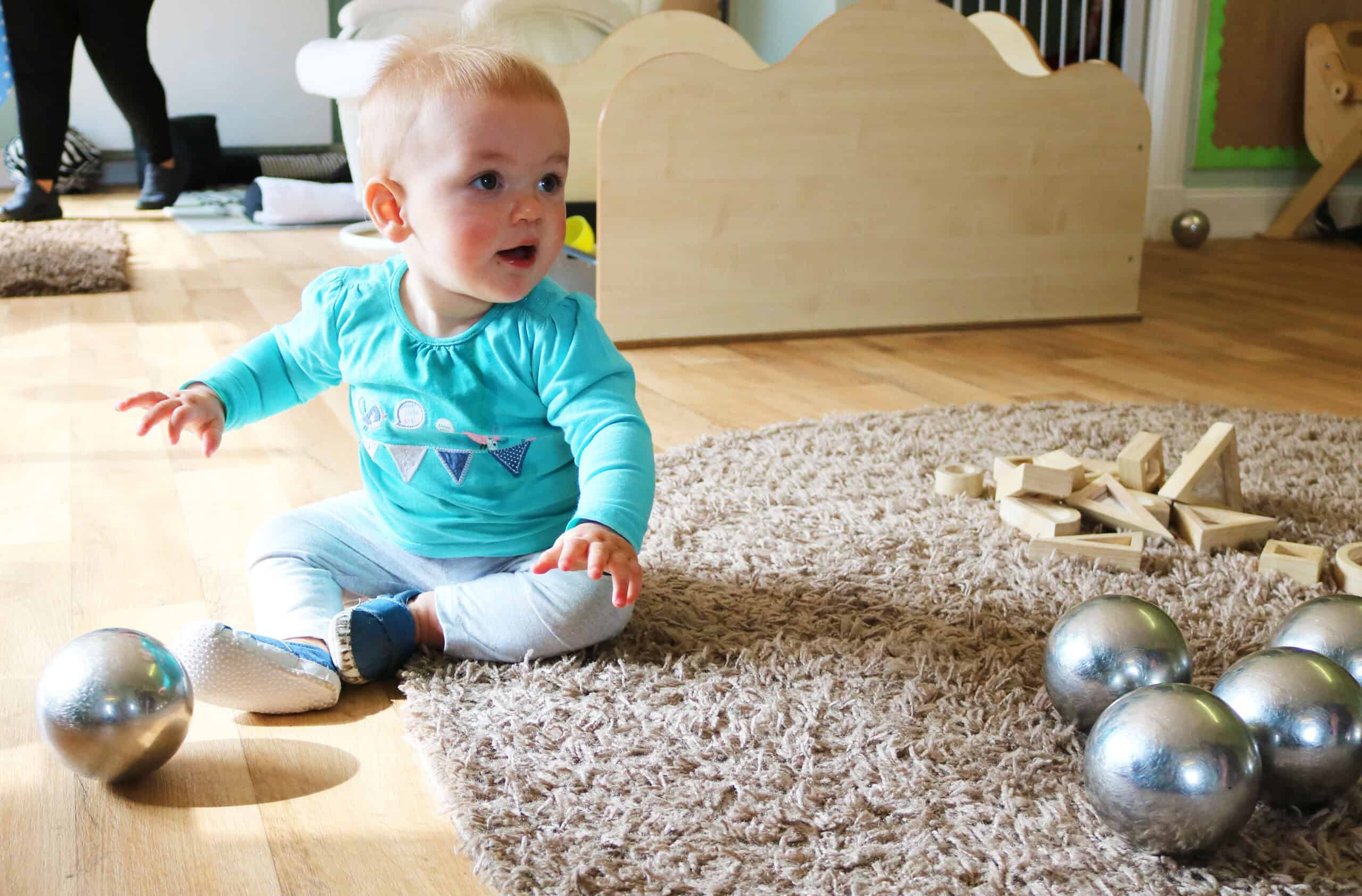 Bright young child playing with metallic balls and wooden building blocks at Thrive Childcare, showcasing a safe and enriching early childhood environment.