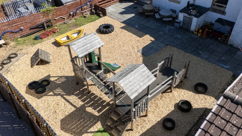 Bright outdoor playground at Thrive Childcare with wooden play structures, tire swings, and sandy play area for children’s fun and active learning.