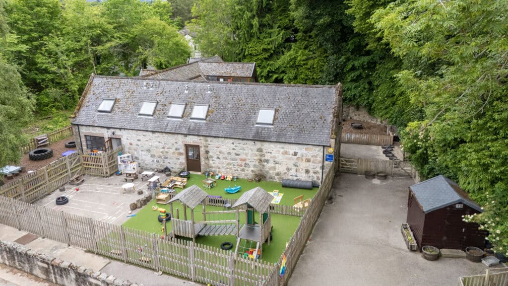 Bright outdoor childcare area at Thrive Childcare, featuring a fenced playground with toys, play structures, and lush green surroundings, perfect for early childhood education and development.