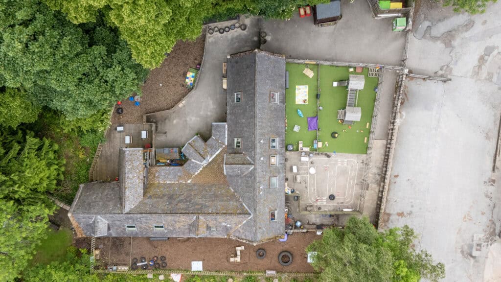 Bright aerial view of Thrive Childcare with outdoor play area, green turf, and surrounding trees, highlighting a safe, engaging environment for early childhood development and learning.