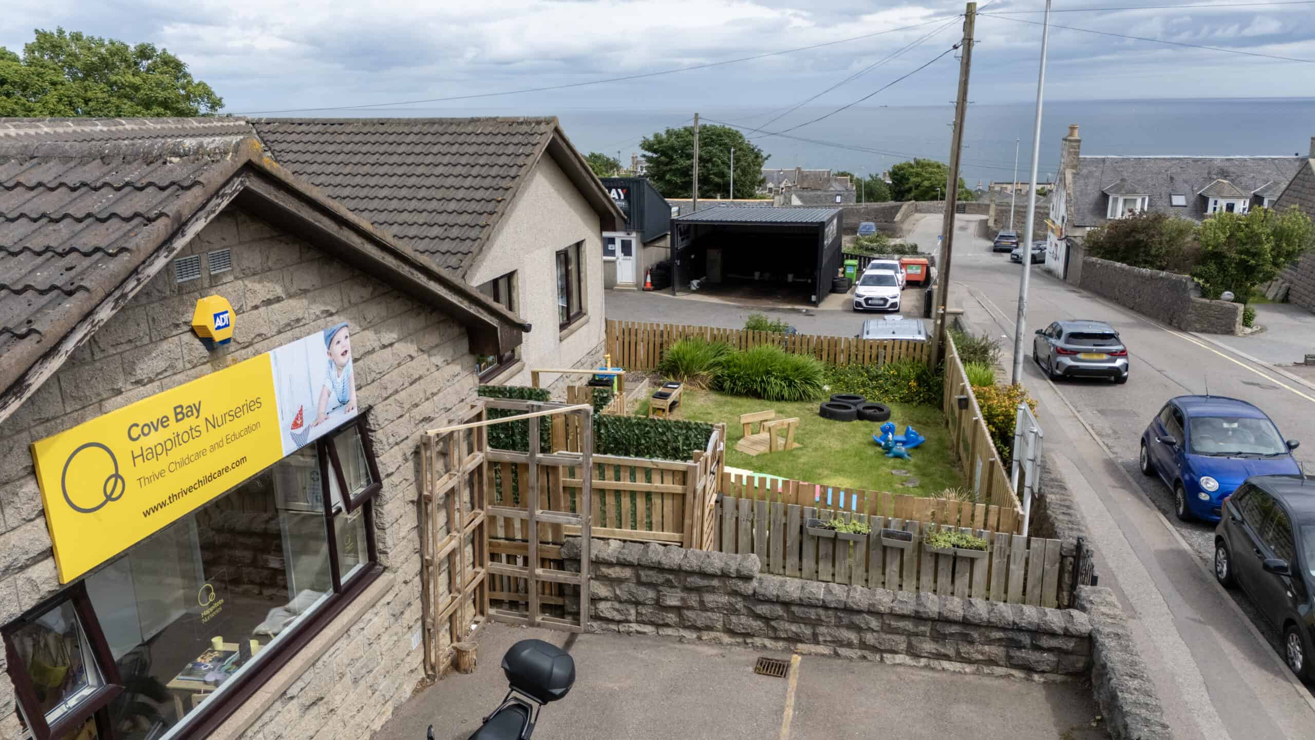 Bright outdoor nursery play area at Thrive Childcare, featuring a secure garden with toys and seating, overlooking a quiet coastal town, ideal for early childhood development and outdoor learning.