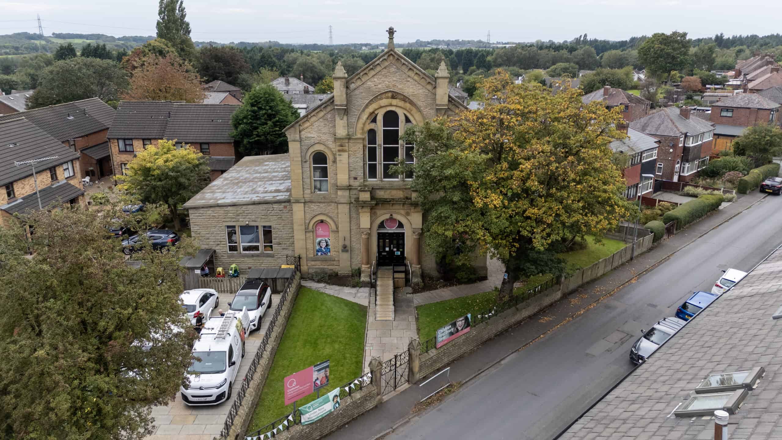 Bright, historic church building with a childcare centre, surrounded by trees and residential houses, promoting nurturing early childhood education in a welcoming community setting.