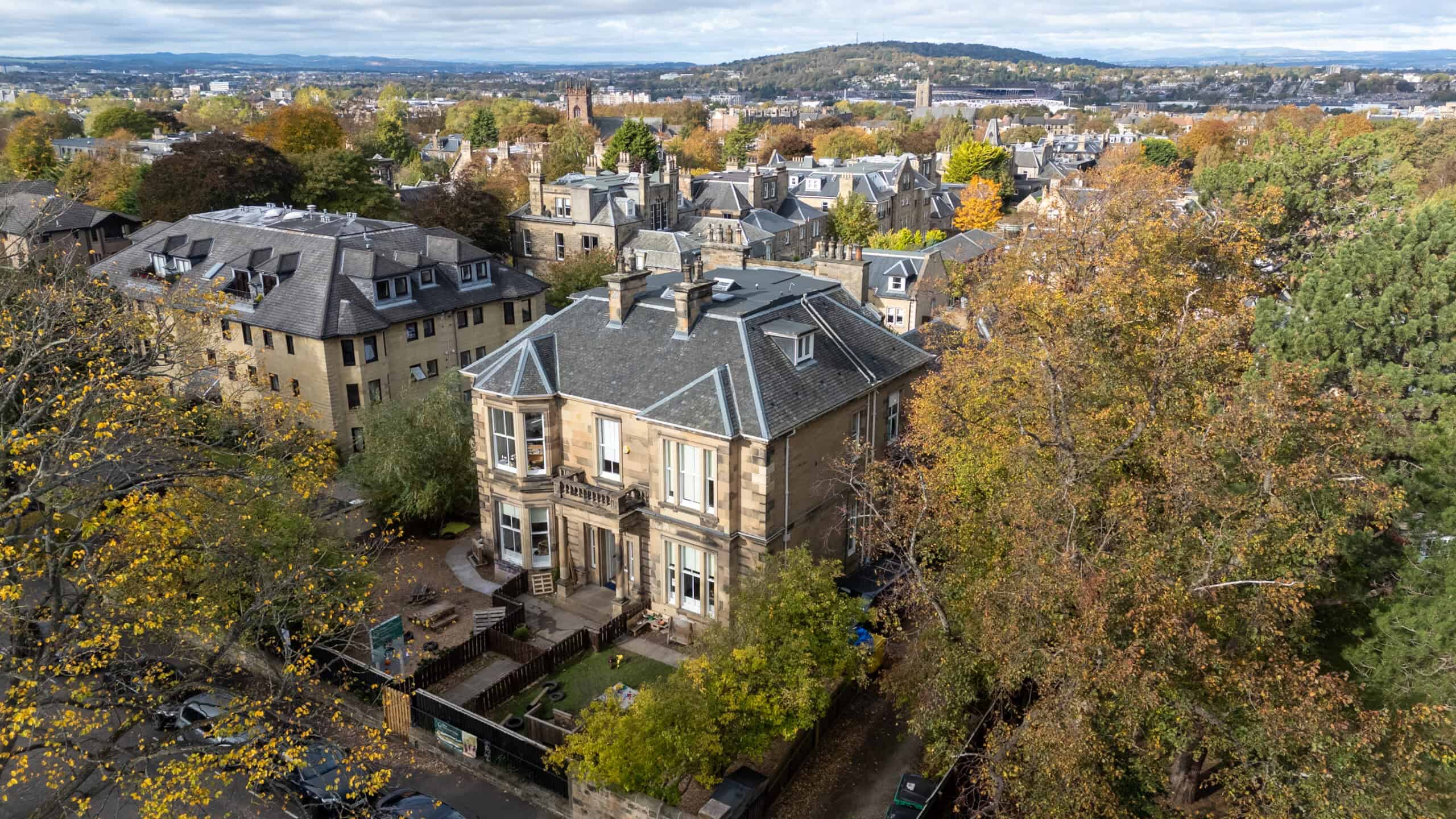 Historic residential building surrounded by trees with autumn foliage in a cityscape, aerial view.