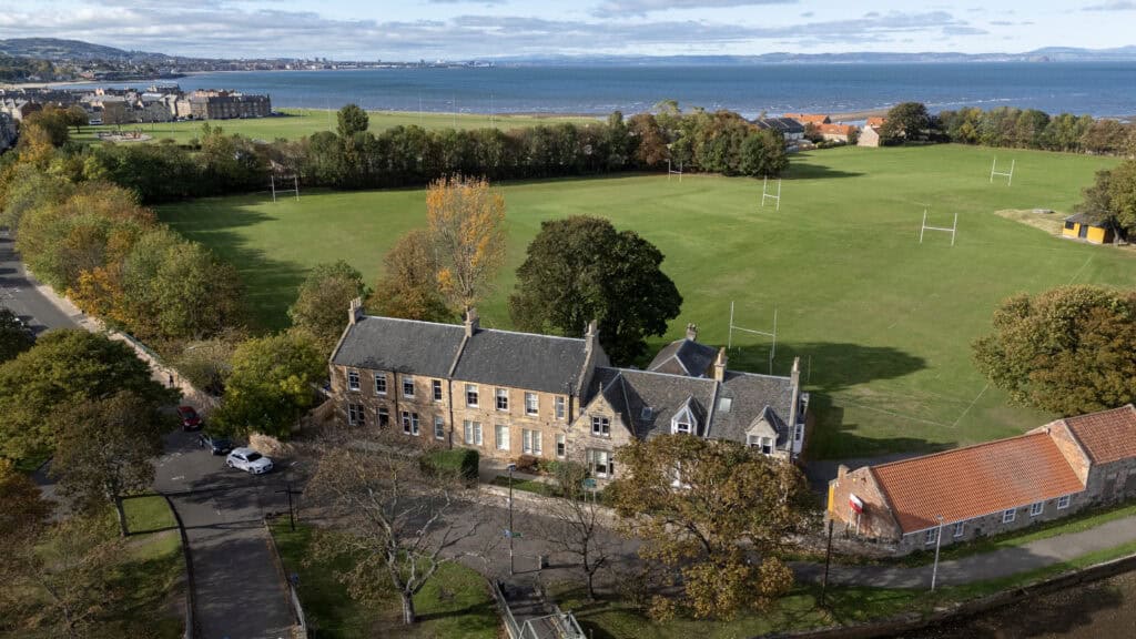 Aerial view of Thrive Childcare centre situated near a large green sports field, overlooking the coastline, with trees and residential buildings highlighting a peaceful community setting.