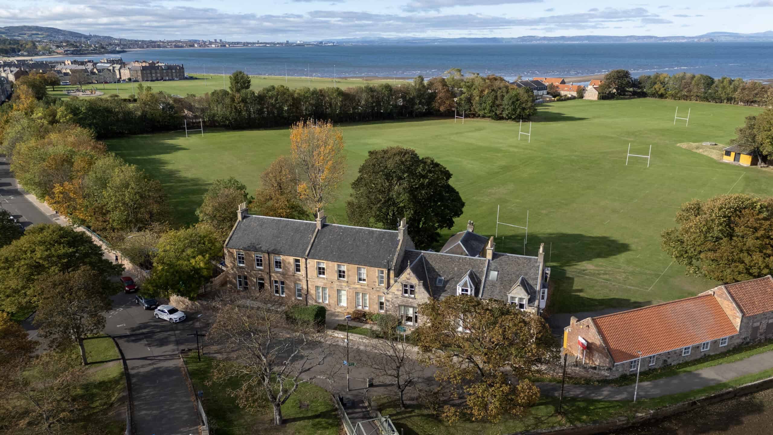 Aerial view of Thrive Childcare centre situated near a large green sports field, overlooking the coastline, with trees and residential buildings highlighting a peaceful community setting.