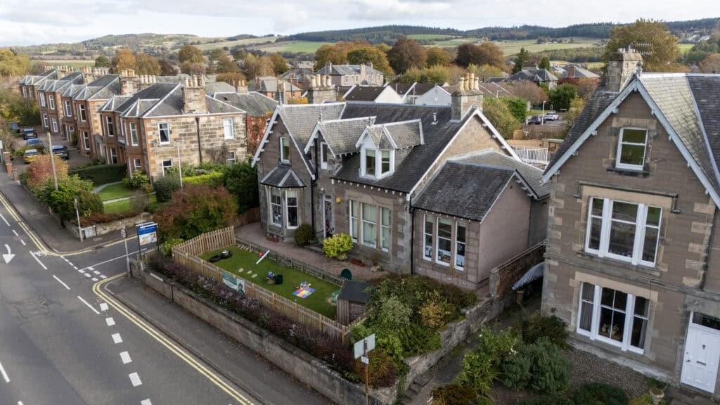 Bright aerial view of Thrive Childcare centre in a historic stone building, surrounded by vibrant greenery and residential neighbourhood, offering quality early childhood education and childcare services in a welcoming environment.