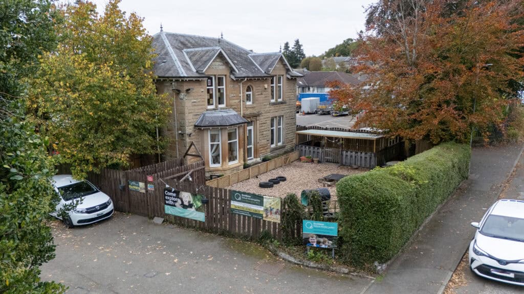 Bright outdoor view of Thrive Childcare with a secure playground, surrounded by trees and fencing, providing a nurturing environment for early childhood education and development in a safe, family-friendly setting.