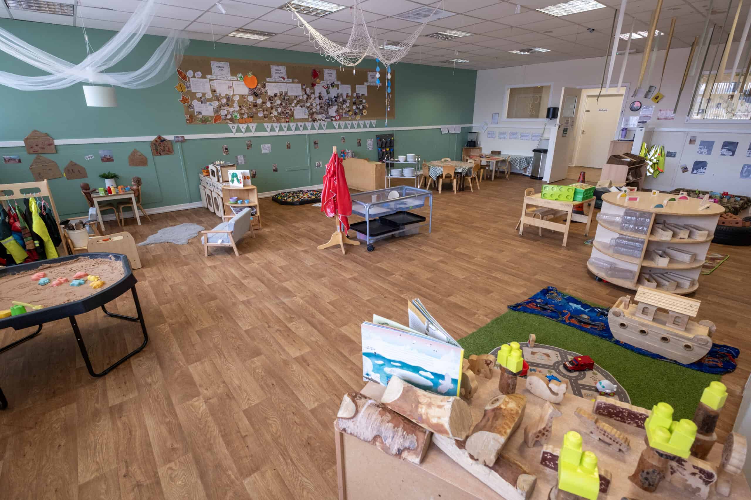 Bright, welcoming Thrive Childcare indoor playroom with diverse activity stations, wooden toys, and cosy reading areas, designed to support early childhood development and learning.
