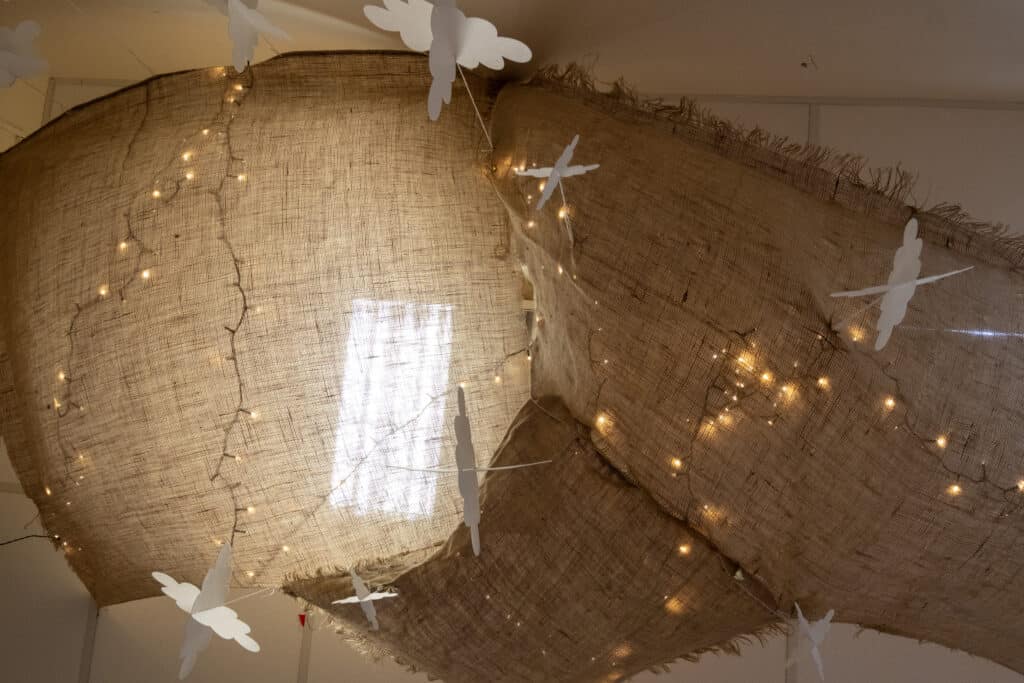 Soft beige fabric canopy decorated with fairy lights and white paper angel cutouts, creating a cosy and calming environment for early childhood development at Thrive Childcare.