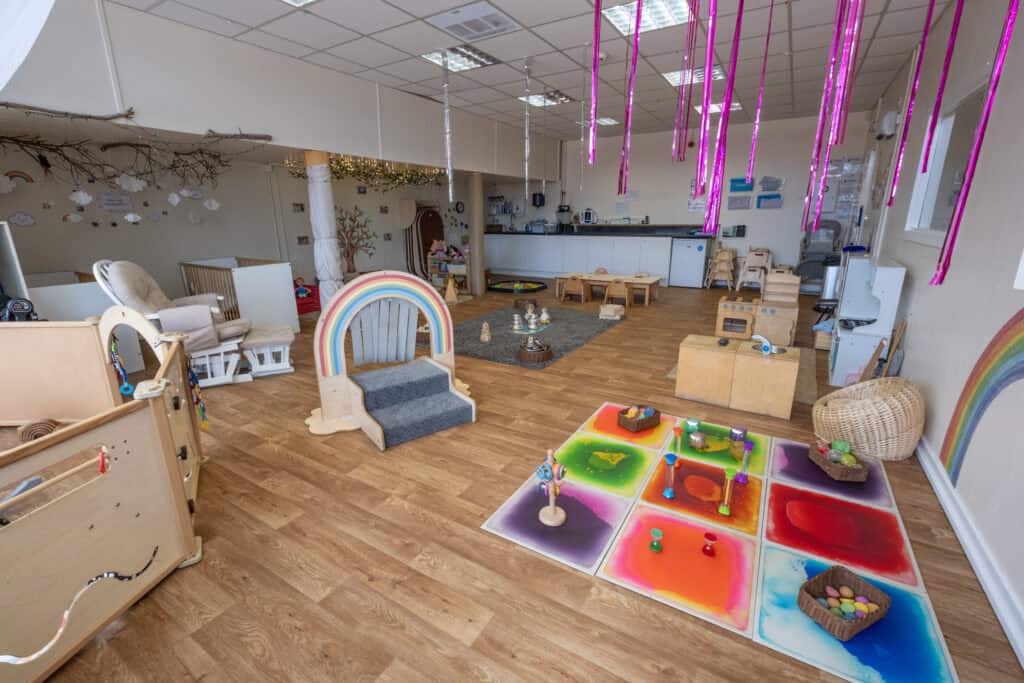 Bright indoor play area at Thrive Childcare with colourful sensory activities, wooden toys, rainbow décor, and age-appropriate furniture, creating a safe, engaging environment for young children.