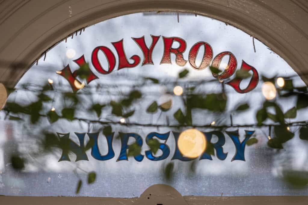 Brightly coloured "Holly Road Nursery" sign visible on a window, with festive holiday decoration and greenery, indicating a welcoming environment for children’s early learning and childcare.