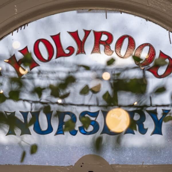 Brightly coloured "Holly Road Nursery" sign visible on a window, with festive holiday decoration and greenery, indicating a welcoming environment for children’s early learning and childcare.