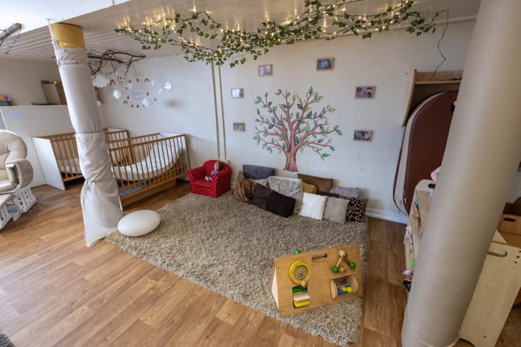 Bright and cosy toddler playroom at Thrive Childcare with soft cushions, climbing frame, and playful wall art, creating a safe and nurturing environment for early childhood development.