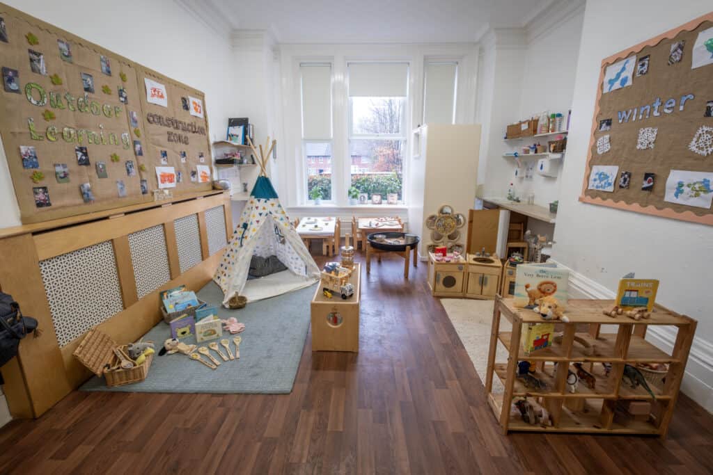 Bright indoor children’s playroom with wooden furniture, toys, books, and educational displays, fostering early childhood development and childcare at Thrive Childcare.