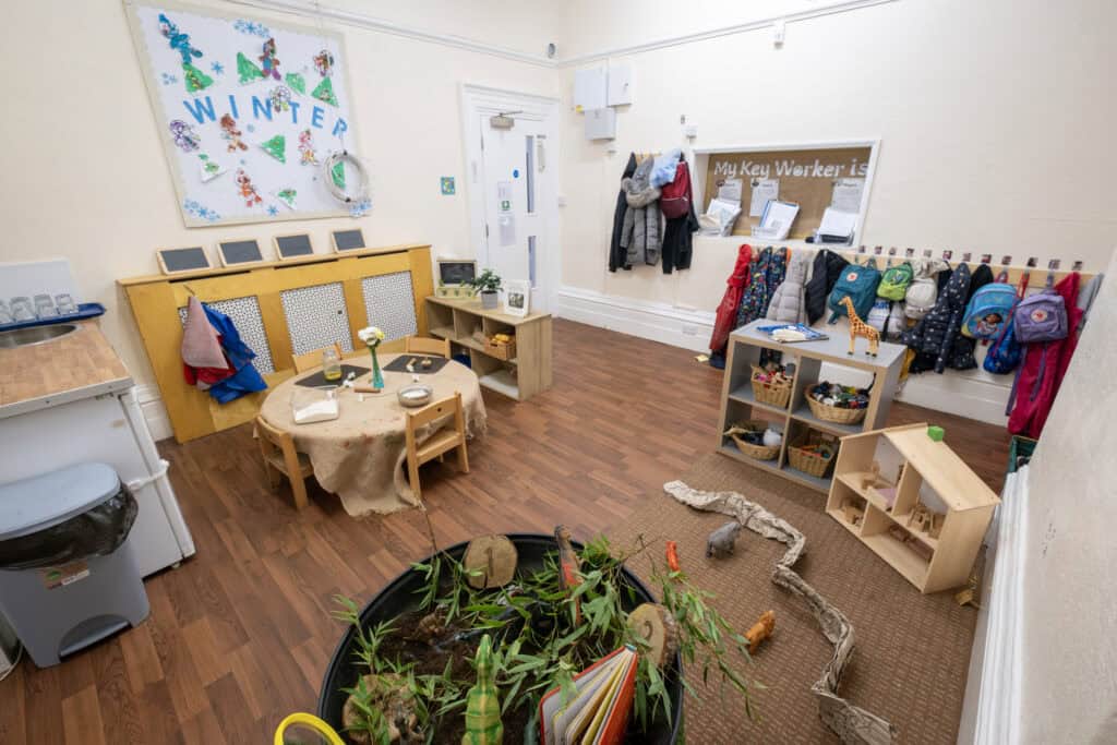 Bright indoor playroom at Thrive Childcare featuring children's coat hooks, educational toys, and a cosy tabletop area for kids' activities, promoting a safe and nurturing environment for early childhood development.