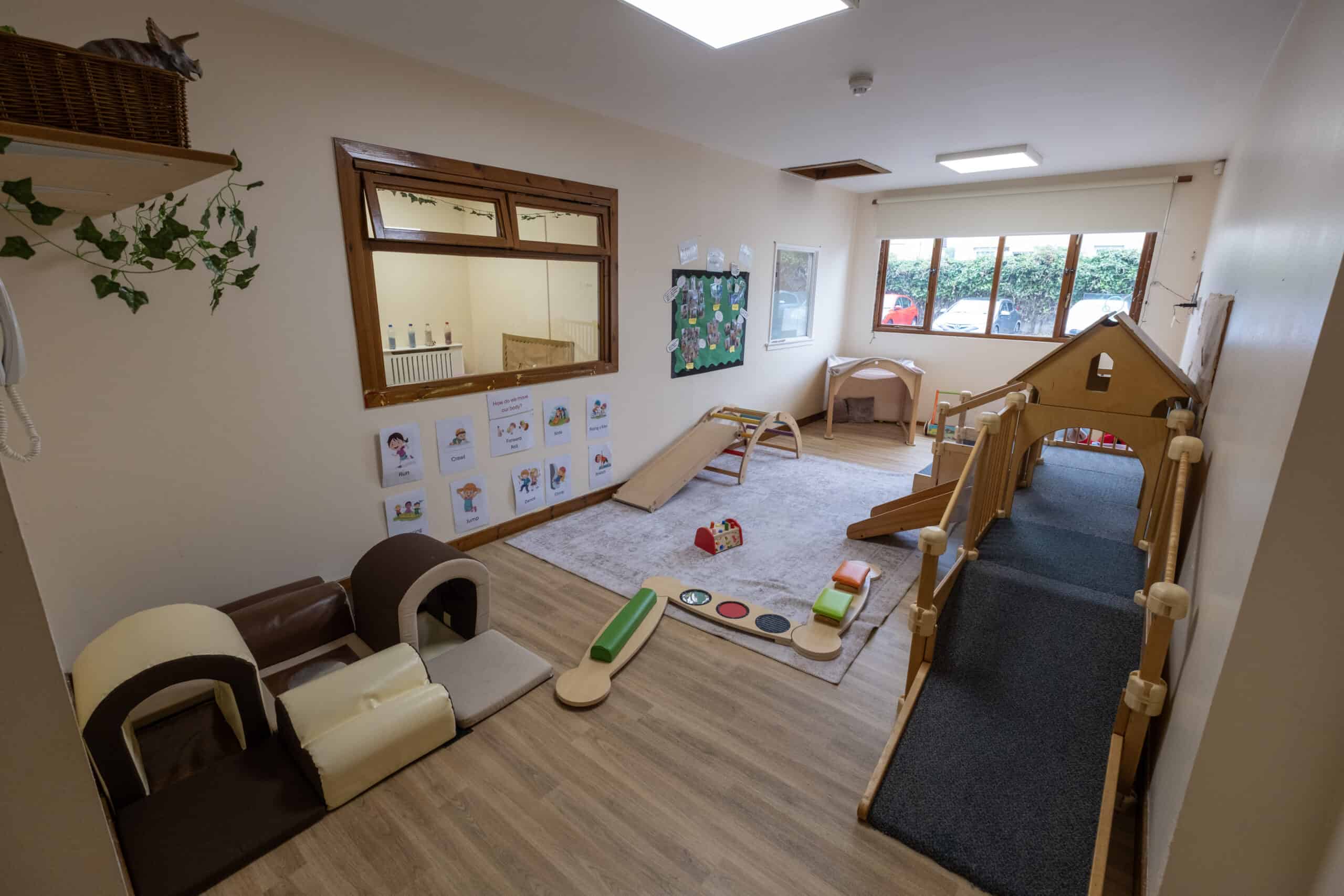 Bright indoor playroom at Thrive Childcare featuring wooden play equipment, soft mats, and educational posters, ideal for early childhood development and childcare activities in a safe, welcoming environment.