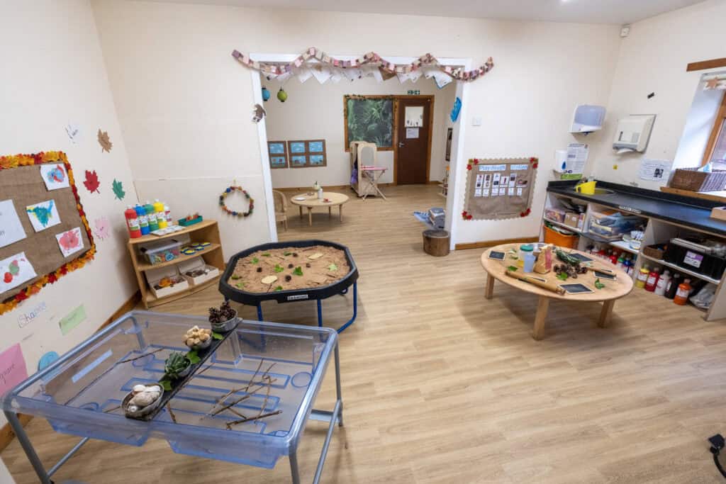 Bright, welcoming childcare playroom with sand table, sensory activities, and creative play stations, designed for early childhood development and engaging learning experiences at Thrive Childcare.