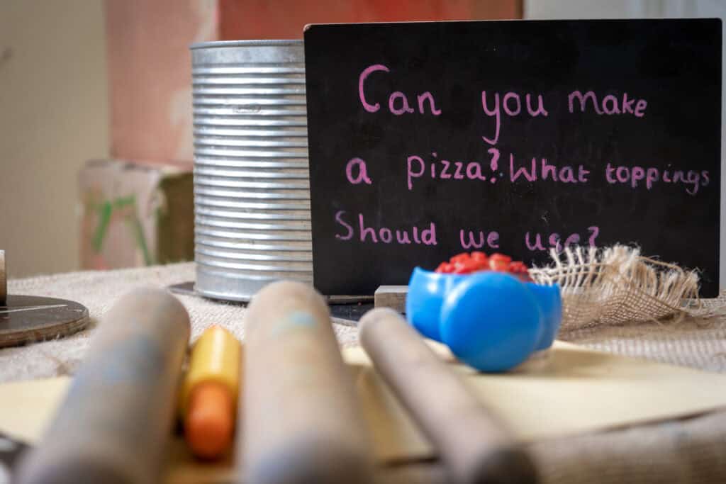 Bright children's play area with a chalkboard asking, "Can you make a pizza? What toppings should we use?" surrounded by craft supplies, emphasizing creative learning at Thrive Childcare.