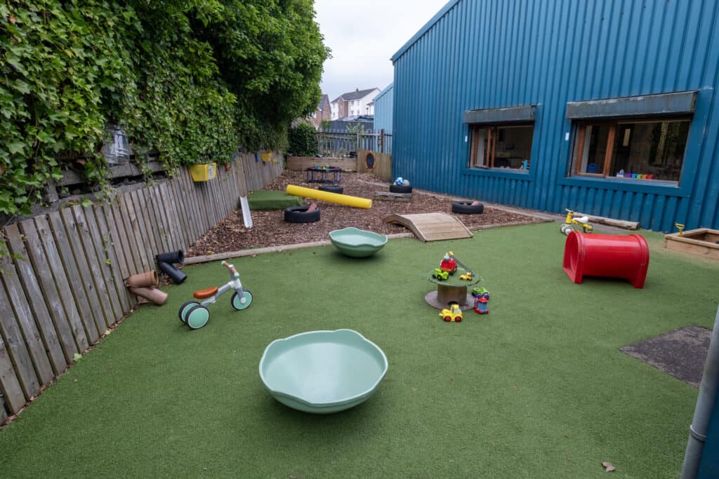 Bright outdoor childcare play area with artificial grass, toys, climbing features, and a safe environment for children at Thrive Childcare. Perfect for early childhood development and outdoor learning.
