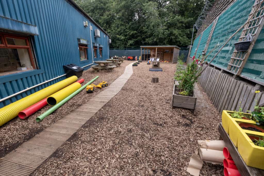 Colourful outdoor play area at Thrive Childcare with natural wood chip ground, garden beds, toys, and play structures for early childhood development and outdoor learning.