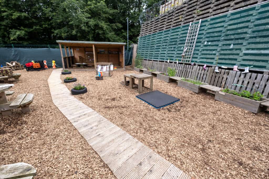 Bright outdoor nursery play area with wood chip flooring, garden planters, and playground equipment, ideal for preschool learning and outdoor activities at Thrive Childcare.