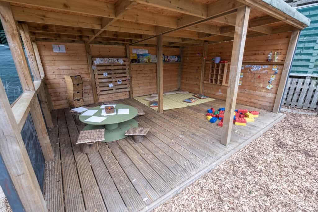 Bright outdoor wooden playhouse with a cozy corner for children’s activities, soft cushions, educational toys, and colourful building blocks, fostering imaginative play and social interaction at Thrive Childcare.