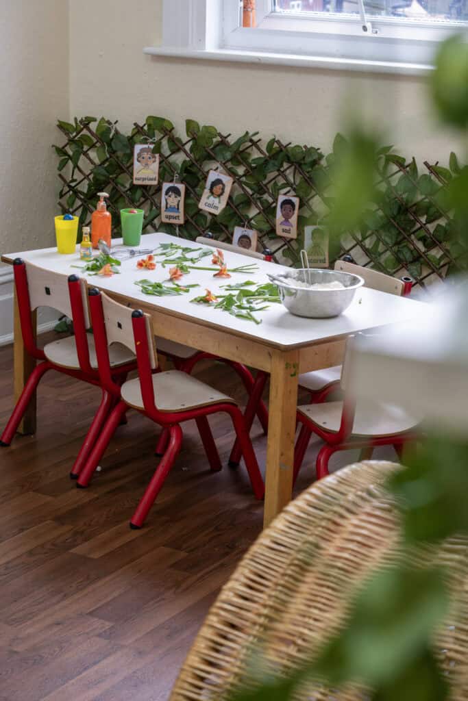 1. Childcare table with flowers, art supplies, and a bowl, in a bright nursery at Thrive Childcare, promoting a nurturing learning environment for young children.