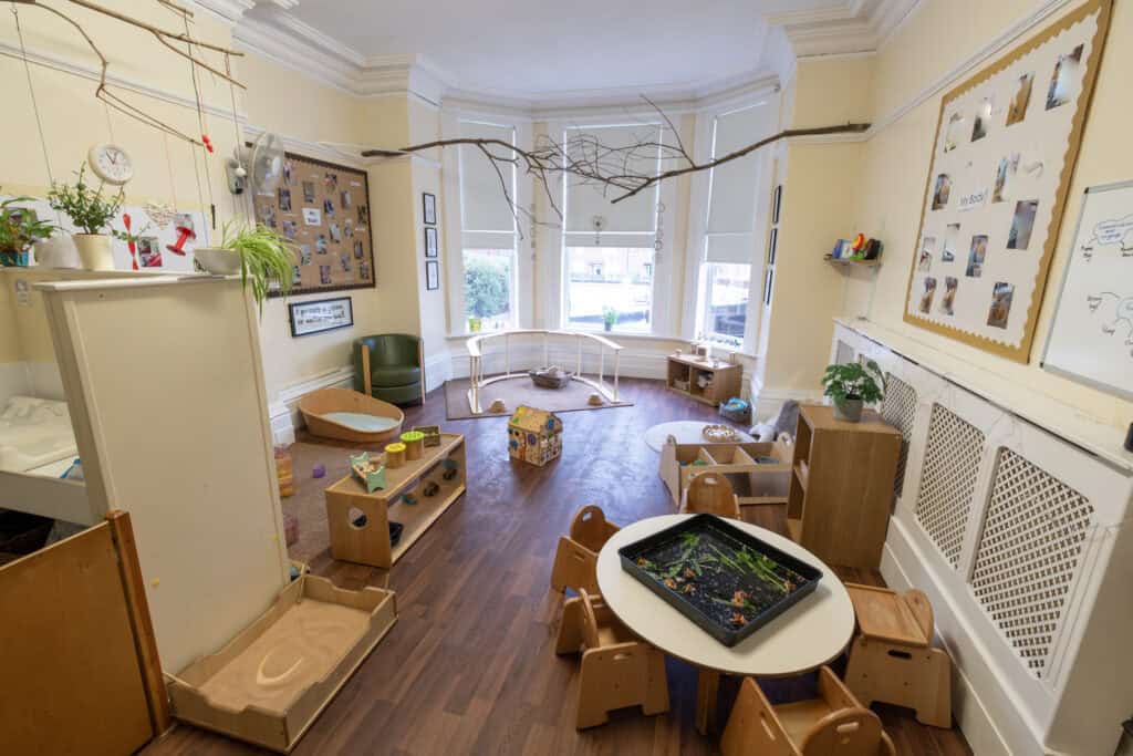 Bright and inviting indoor toddler playroom with natural light, wooden toys, sensory activities, and cosy reading corners, designed to promote early childhood development and learning at Thrive Childcare.