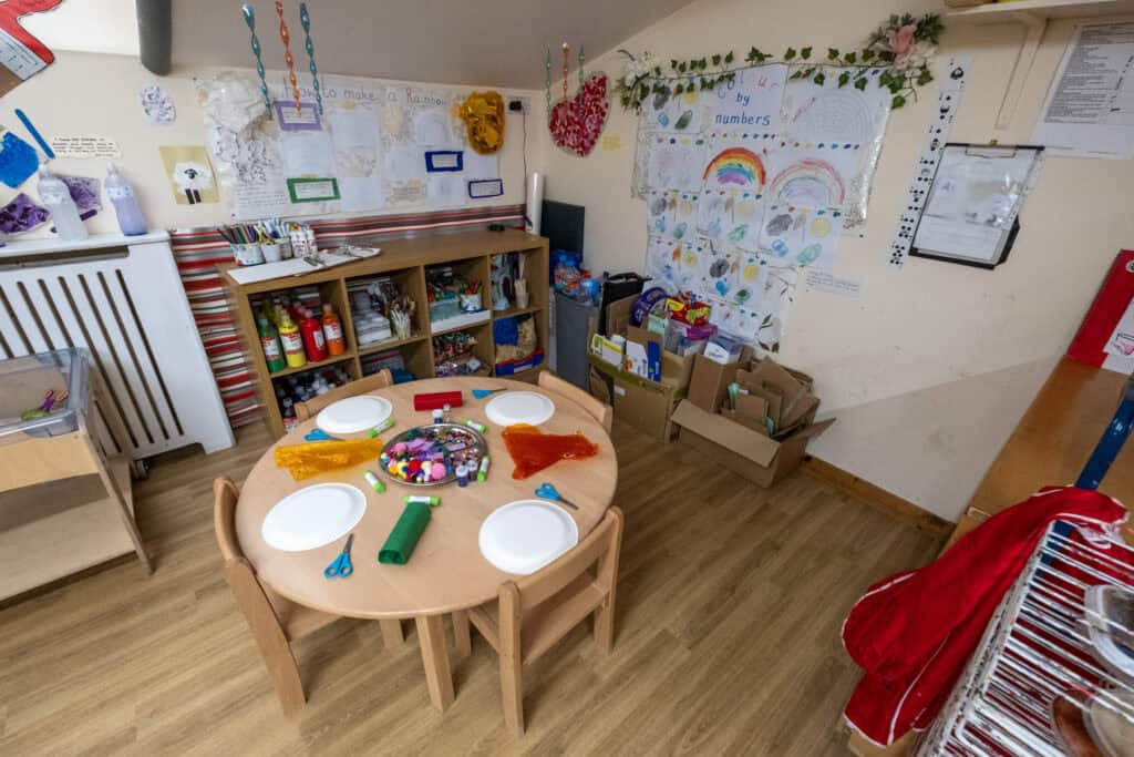 Bright indoor preschool craft area with a round table set for children’s activities, surrounded by art supplies, colourful decorations, and educational artworks, perfect for early childhood development.