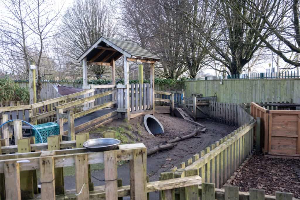 Bright outdoor childcare play area with wooden climbing structures, tunnels, and natural play elements for young children at Thrive Childcare.