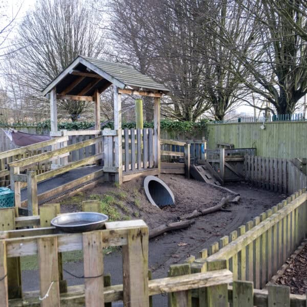 Bright outdoor childcare play area with wooden climbing structures, tunnels, and natural play elements for young children at Thrive Childcare.