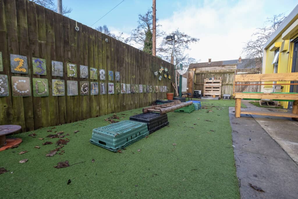 Bright outdoor childcare play area at Thrive Childcare, featuring colourful educational wall art, step platforms, and secure fencing, designed for early childhood development and safe fun.
