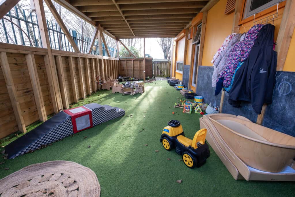 Bright outdoor play area at Thrive Childcare with artificial grass, toys, and play equipment, providing a safe, engaging environment for young children.