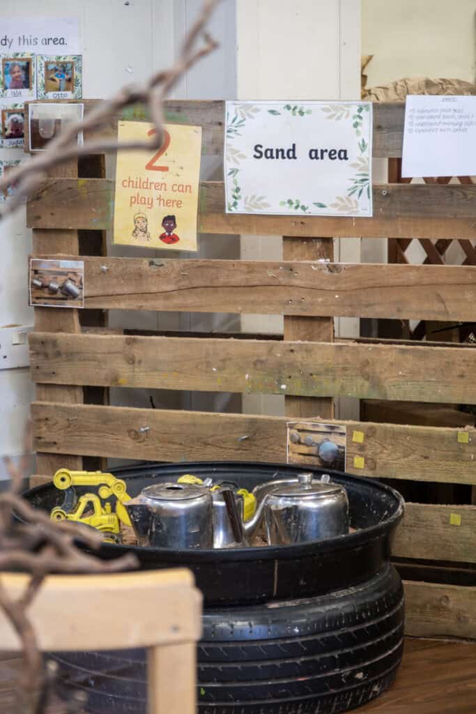 1. Brightly lit sand play area at Thrive Childcare with wooden fencing and educational signs for children’s outdoor learning activities.