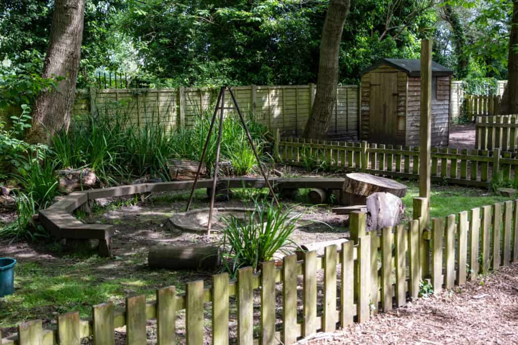 A peaceful outdoor play area at Thrive Childcare with natural elements, trees, and a wooden shed, promoting outdoor learning and exploration for young children in a safe environment.