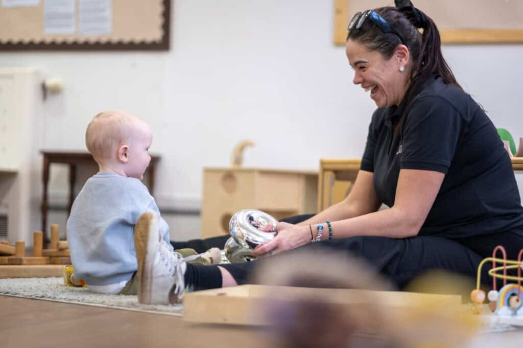 Brightly smiling nursery staff engaging with happy toddler during playtime at Thrive Childcare in a welcoming early years education environment.