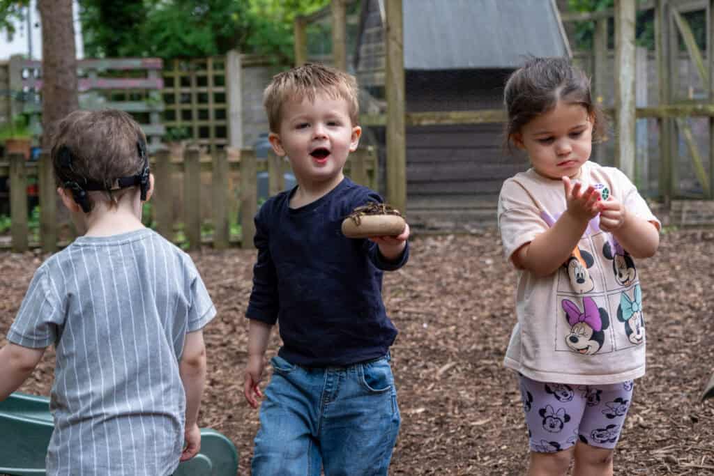 Children playing outdoors at Thrive Childcare nursery, engaging in hands-on activities in a natural environment, promoting development, exploration, and fun.