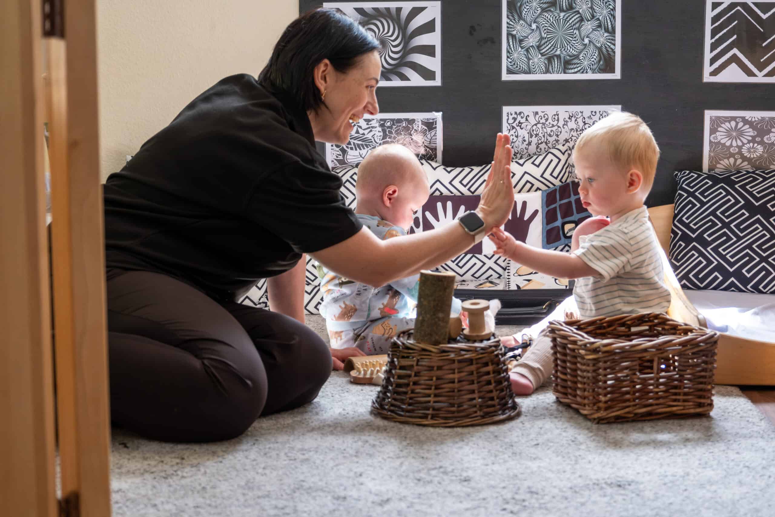 High-quality image of a caregiver engaging with two young children in a colourful, educational nursery setting at Thrive Childcare, supporting early childhood development and nurturing a friendly learning environment.