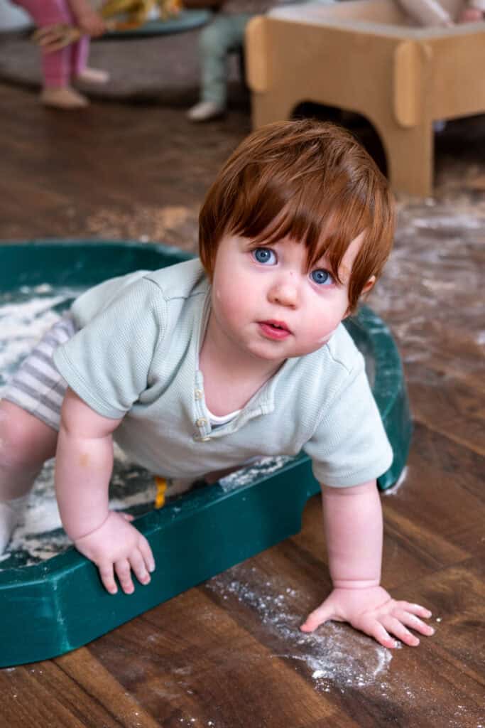 1. Young child playing and crawling in a sensory activity tray at Thrive Childcare, promoting early childhood development and engagement.