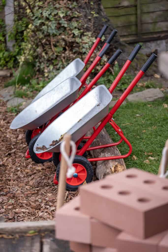 Children's outdoor play area at Thrive Childcare with wheelbarrows and bricks, encouraging physical activity and creativity in a safe environment.