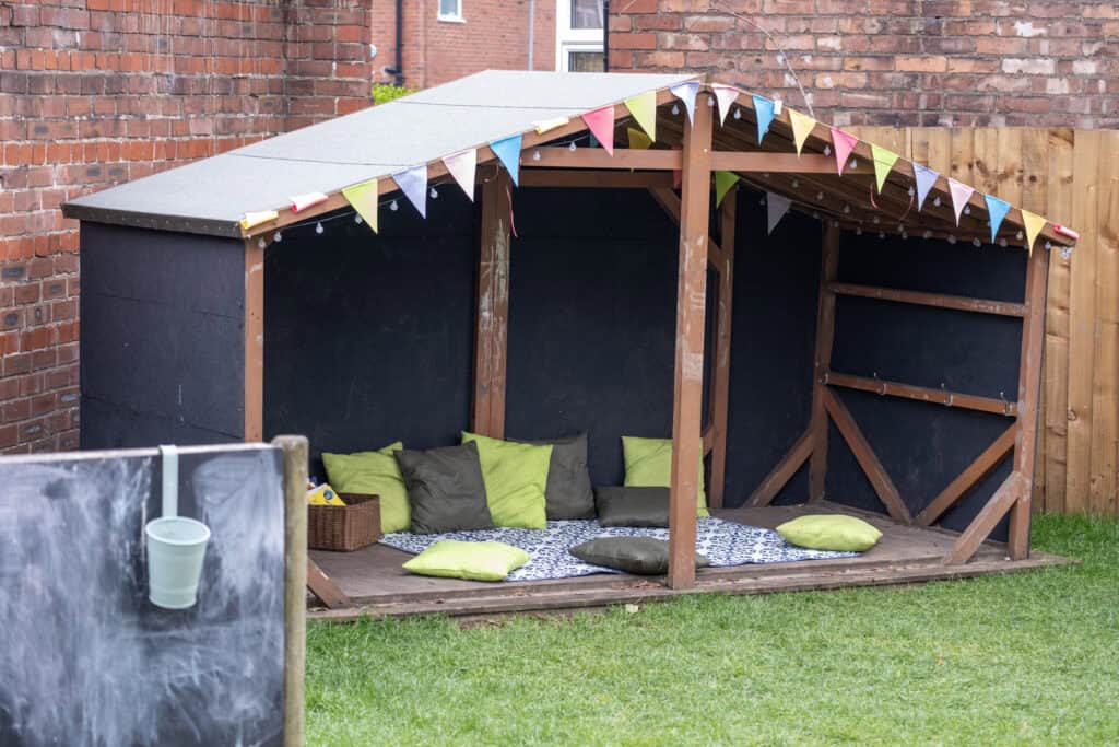 A colourful outdoor children's playhouse with cushions and a cozy corner for kids to relax and enjoy outdoor activities, ideal for early childhood education and outdoor play.