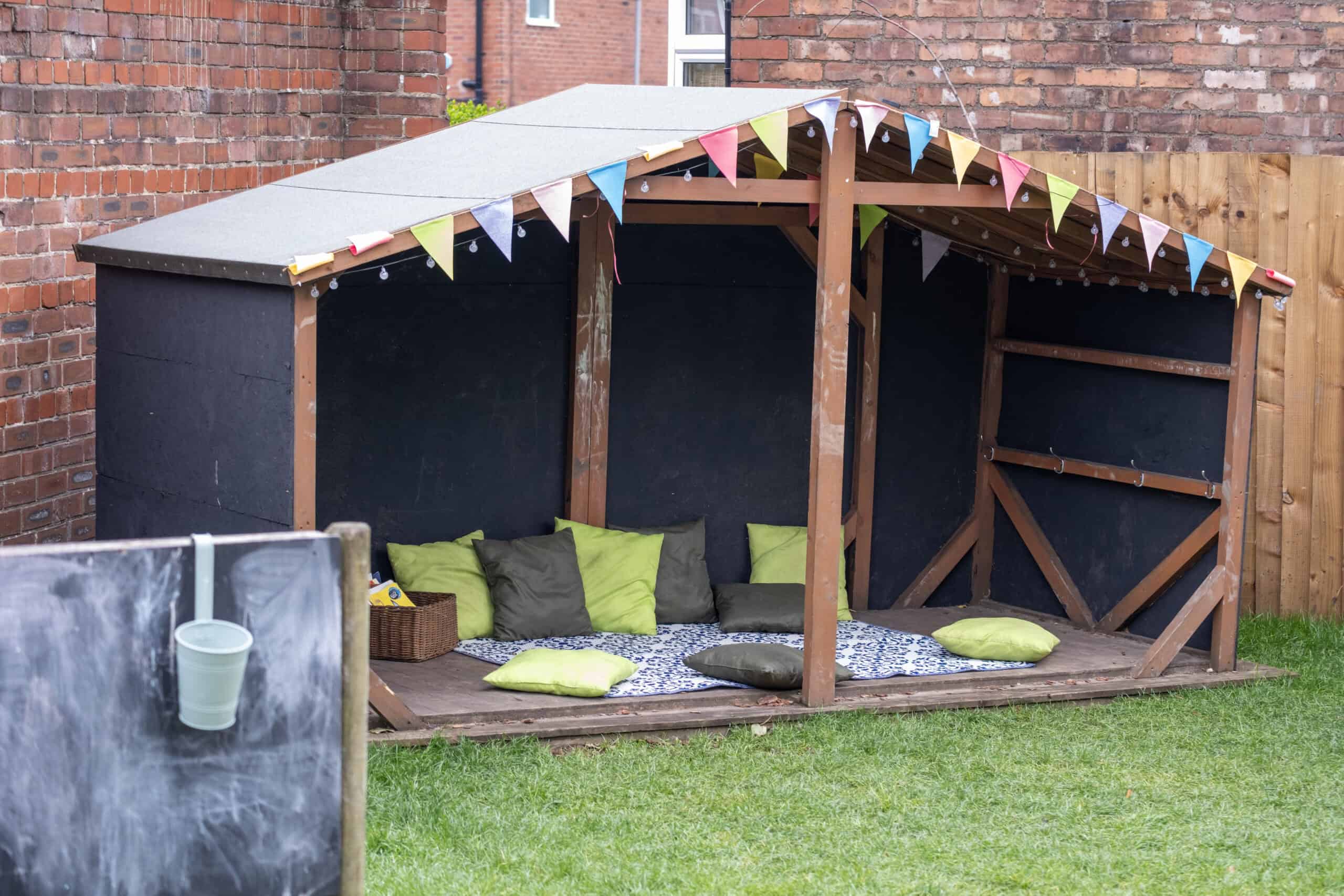 A colourful outdoor children's playhouse with cushions and a cozy corner for kids to relax and enjoy outdoor activities, ideal for early childhood education and outdoor play.