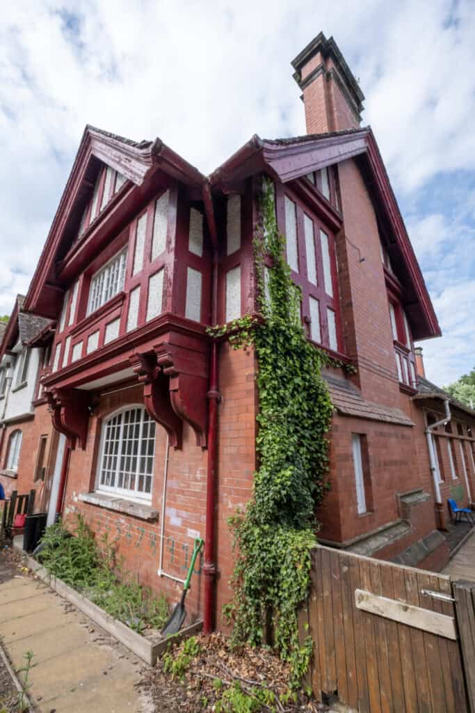 Bright, historic red brick building with Tudor-style timber framing, part of Thrive Childcare facility, under a partly cloudy sky, surrounded by greenery and garden tools; a welcoming environment for children.