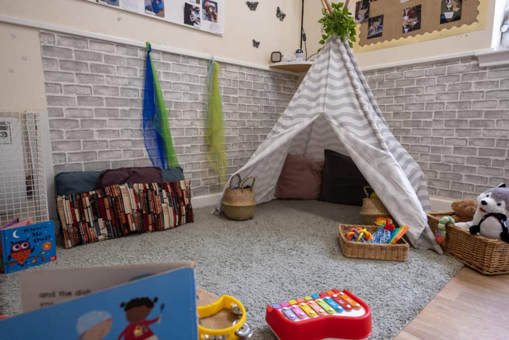 Soft play area featuring a white striped teepee tent, colourful toys, cushions, and children's books, ideal for early childhood development at Thrive Childcare.